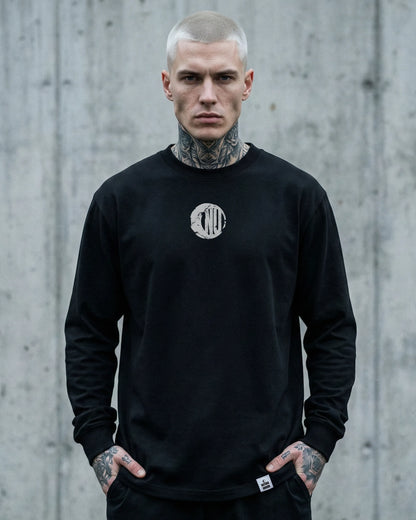 Männliches Model trägt Stanley/Stella Freestyler Longsleeve T-Shirt in Schwarz mit "Natura Umbra" Frontprint – nachhaltige Unisex Streetwear.