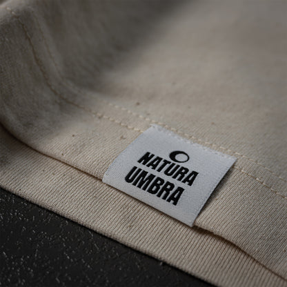 Nachhaltiges T-Shirt in Natural Raw von Natura Umbra – Detailansicht des gewebten Markenetiketts am linken Saum.