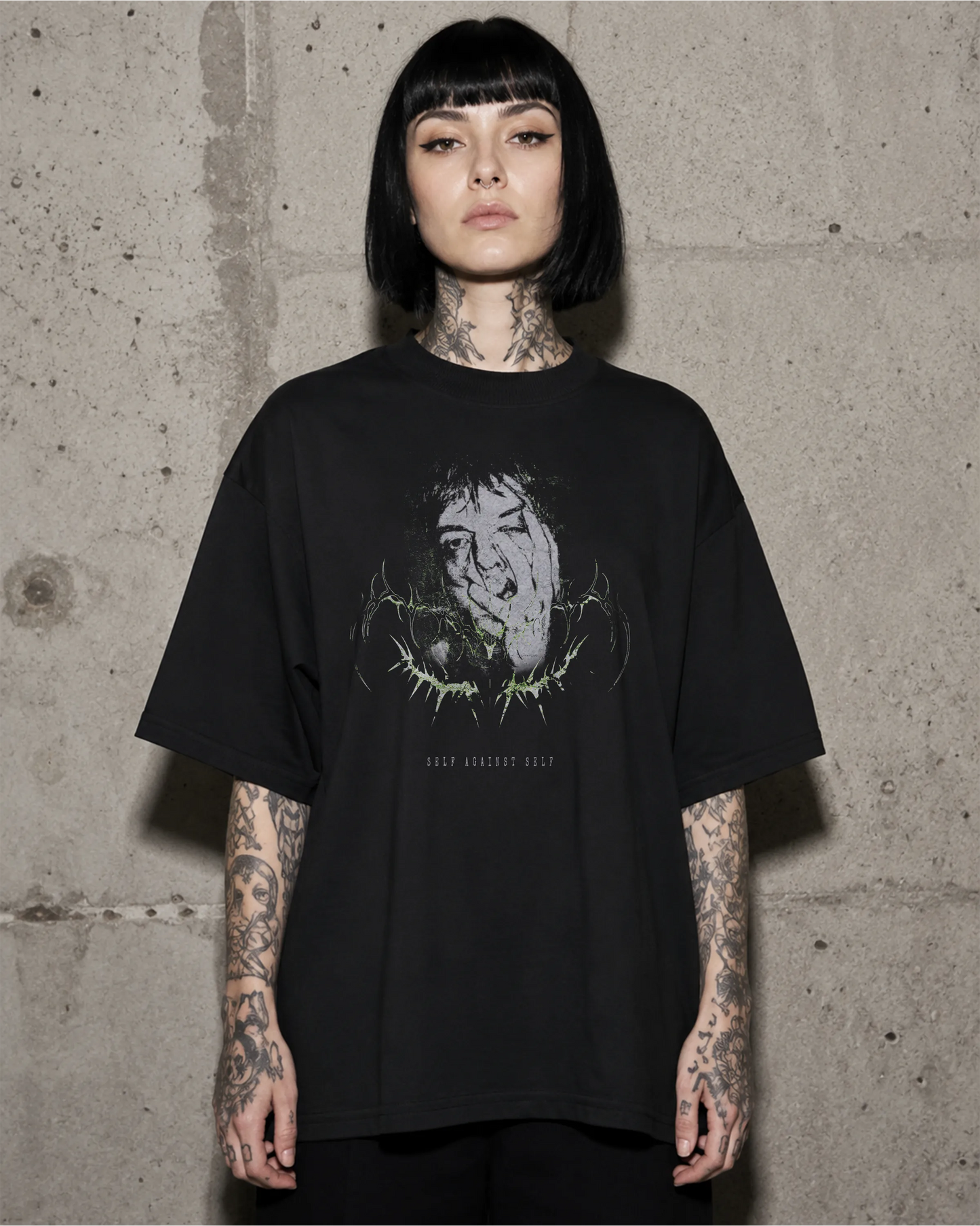 Frau trägt schwarzes SELF AGAINST SELF Oversized T-Shirt vor einer Betonwand.