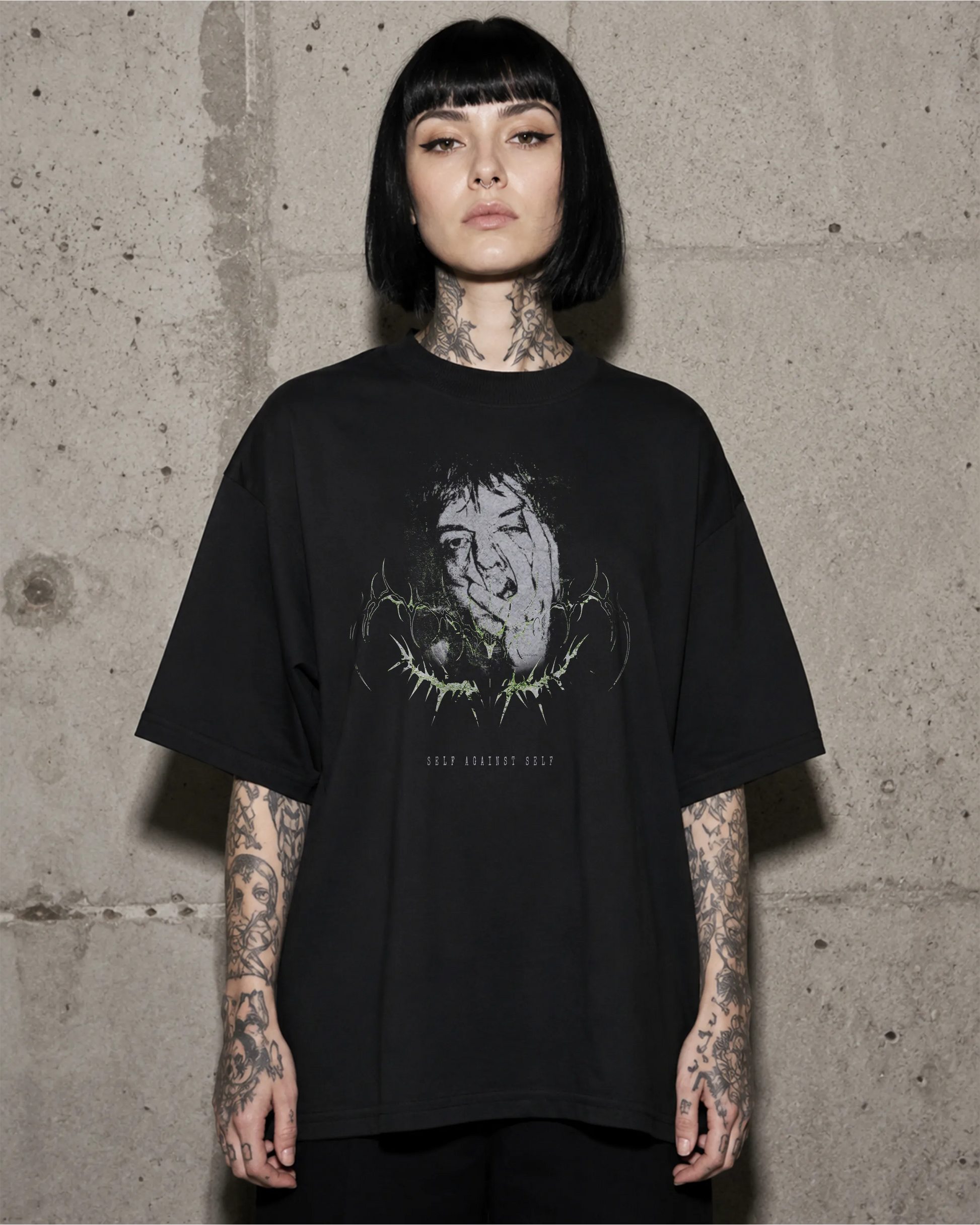 Frau trägt schwarzes SELF AGAINST SELF Oversized T-Shirt vor einer Betonwand.