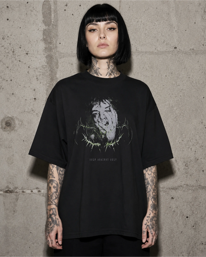 Frau trägt schwarzes SELF AGAINST SELF Oversized T-Shirt vor einer Betonwand.