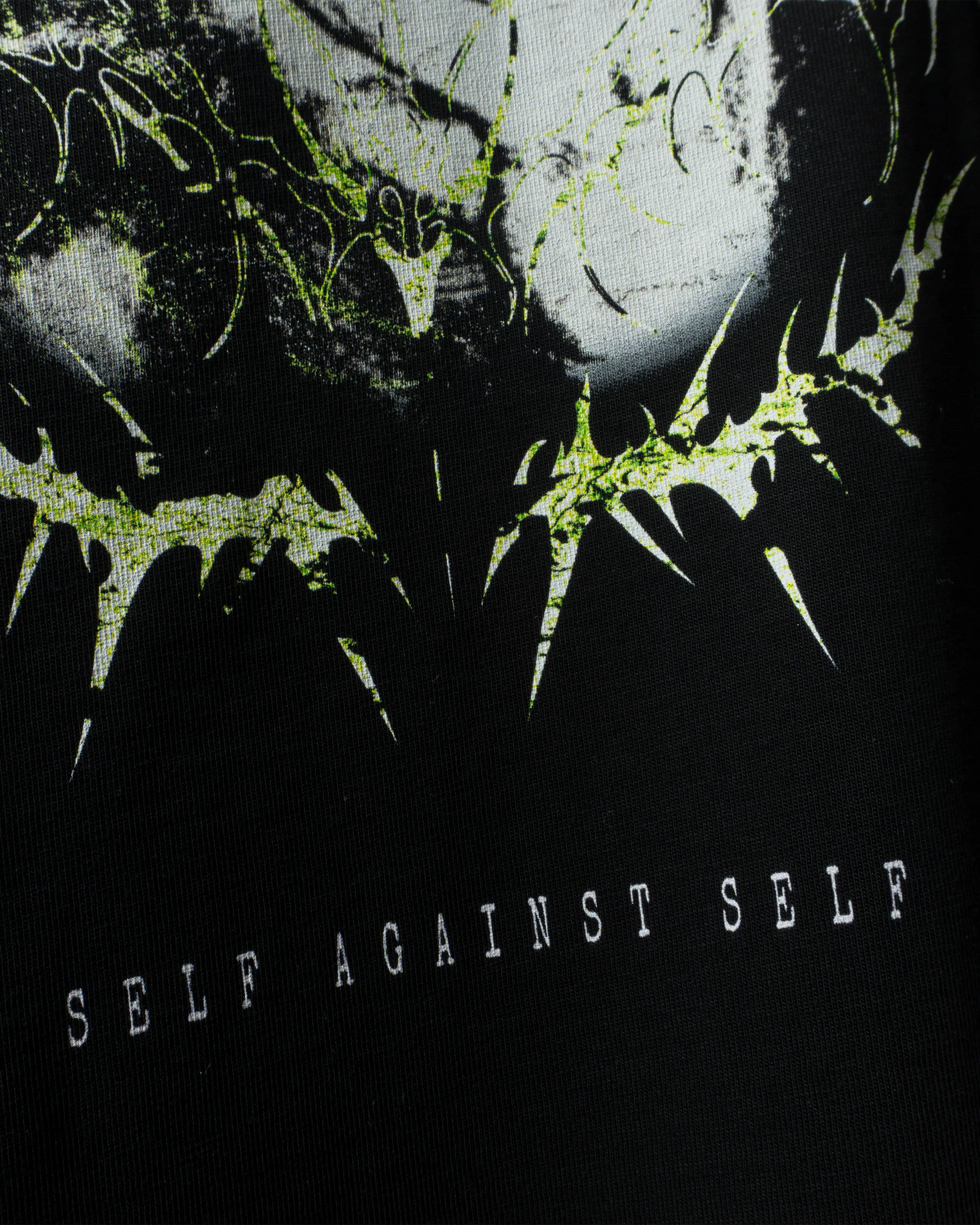 Detailaufnahme des „Self Against Self“-Drucks in Schwarz, Weiß und Neongrün auf schwarzem T-Shirt-Stoff.